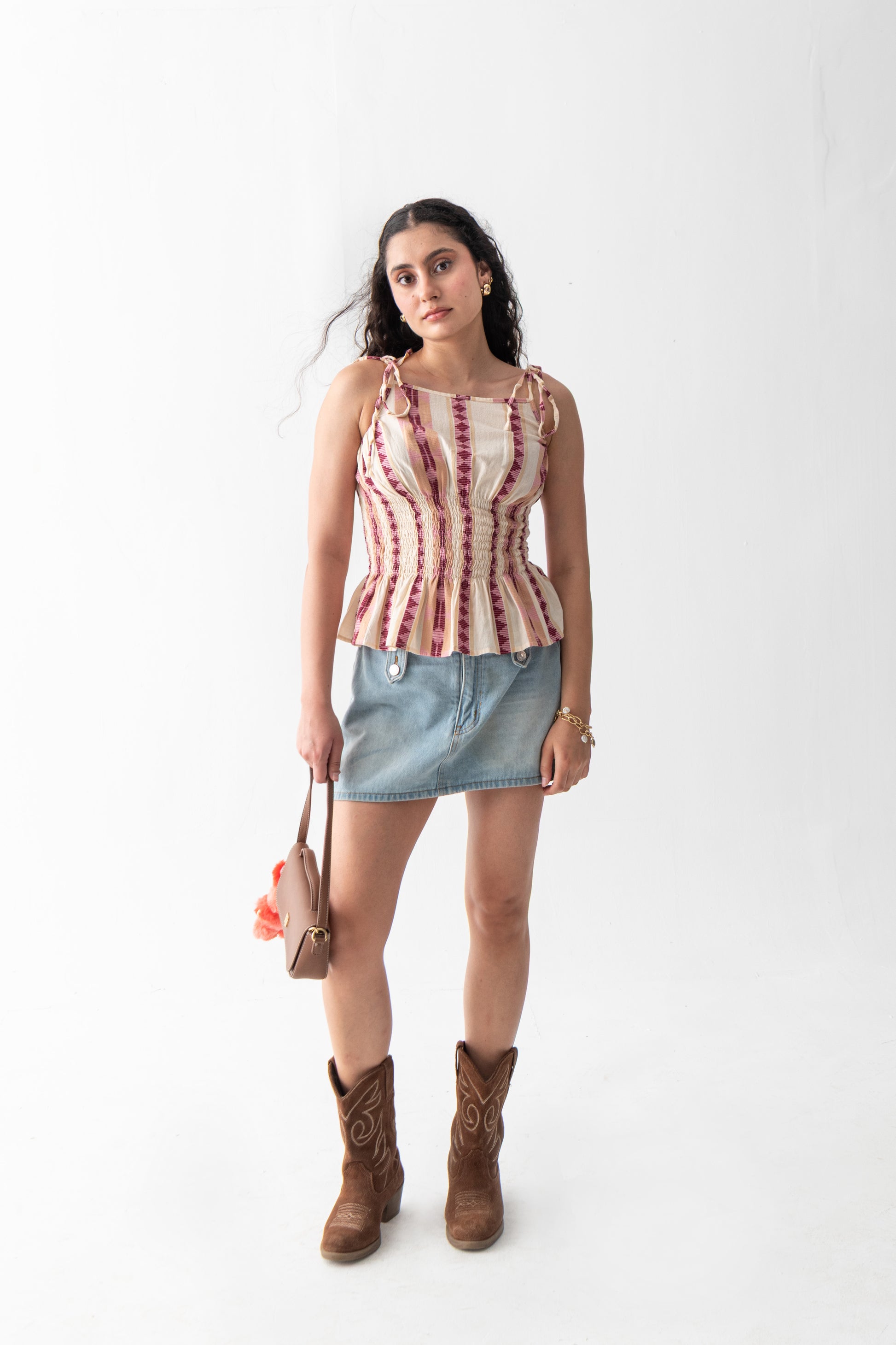 Woman wearing a pink
 and white striped tank top, denim skirt, and brown boots on a white background